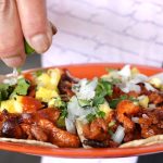 Hand squeezing lime juice on plate of tacos