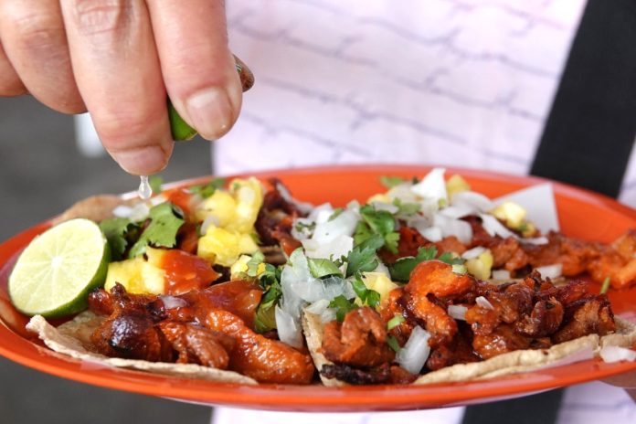 Hand squeezing lime juice on plate of tacos