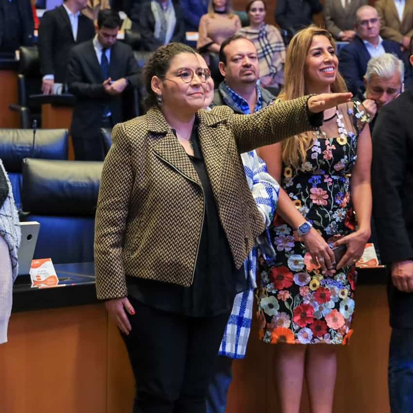 A woman salutes in a congressional hall with a crowd seated behind her
