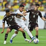 Two Mexican soccer players in red uniforms go after an Ecuadorian player in white with the ball, before Mexico was eliminated from the Copa América.