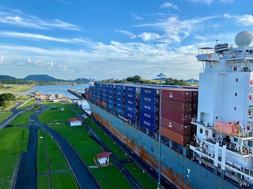 A loaded cargo shipping container enters a narrow canal